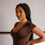 Woman with long box braids wearing a rust‑colored sleeveless top, styled by Braids by Blexin.