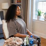 Woman with natural hair seated beside a table of braid essentials, preparing for a professional braid appointment at home.