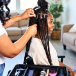 Professional mobile braider styling long box braids for a client at home, with clean tools and a relaxed atmosphere.